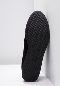 Chaussure en daim noir avec une semelle en caoutchouc texturée, affichant un motif tissé. Étiquette de taille "37" visible sur le côté de la semelle.