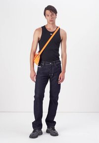 Top sin mangas negro, jeans azul oscuro y zapatos grises. Presenta un bolso cruzado naranja brillante para contraste. Diseño simple y moderno.