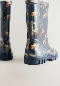 Bottes de pluie en caoutchouc bleues avec un motif coloré de divers véhicules de construction. Semelle épaisse avec grip texturé. Design de hauteur intermédiaire.