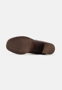 Semelle de chaussure en cuir marron avec une accroche texturée au talon et à l’avant, vue du dessous sur un fond blanc uni.