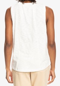 Mouwloos wit topje met een gestructureerd patroon. Heeft een geraffineerde halslijn en een subtiele zoomdetail. Zachte stof met een ontspannen pasvorm.