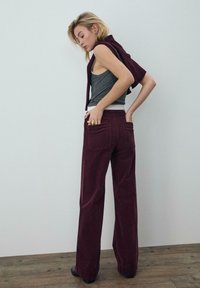 Sztruksowe, bordowe spodnie dzwony z tylnymi kieszeniami, zestawione z szarą koszulką na ramiączkach. Gładka faktura, luźny krój i delikatne detale przeszyć.