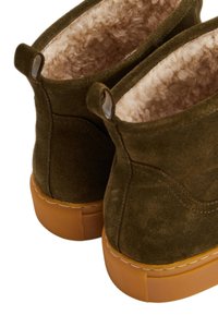 Bottines en daim vert olive avec une doublure beige douce et une semelle en caoutchouc texturée, dotées de deux languettes bouclées pour un enfilage facile.