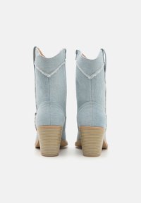 Světle modré denimové kotníkové boty s texturovaným povrchem, podpatkem ze smetanové barvy a třepícími se okraji u kotníku. Zapínání na zip na boku.
