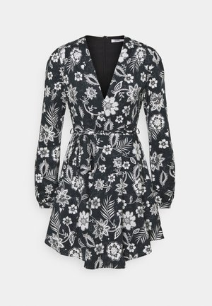 Robe noire à manches longues avec motif floral et feuilles blanches, encolure en V, taille cintrée avec ceinture à nouer et jupe évasée.
