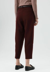 Bordeauxrode broek met een getailleerd ontwerp, korte pijpen en twee achterzakken. Voorzien van een zwarte riem en gecombineerd met zwarte loafers.