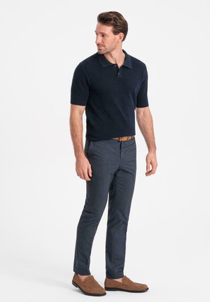 Polo de manga corta en color azul marino con un diseño de tejido texturizado, combinado con unos pantalones oscuros grises ajustados y mocasines marrones.