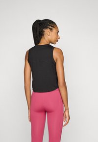 Svart ärmlös topp med rundad halsringning, med en horisontell söm över ryggen. Matcher med åtsittande rosa leggings.