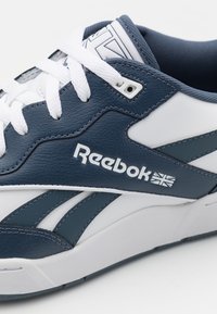 Detailní záběr na námořnickou a bílou tenisku Reebok s bílými tkaničkami a logem Union Jack na bočním panelu.