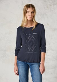 Marineblaues Langarmshirt mit Rundhalsausschnitt, das geometrische Ausschnitte und weißen Text aufweist. Weicher Stoff mit lockerem Schnitt.