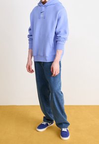 Lilac hoodie with a kangaroo pocket and adjustable drawstring. Paired with light blue loose-fitting jeans and blue sneakers.