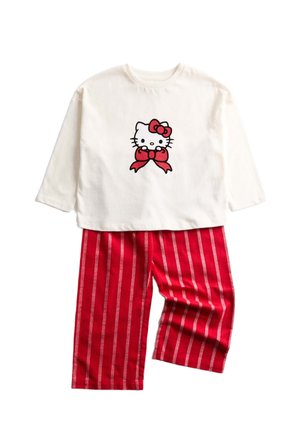 Maglietta a maniche lunghe bianca con grafica di Hello Kitty e fiocco rosso, abbinata a pantaloni rossi a righe con linee verticali bianche.