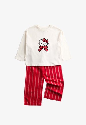 Biały top z długim rękawem z grafiką Hello Kitty i czerwonym kokardą, połączony z czerwonymi spodniami w paski z białymi pionowymi liniami.