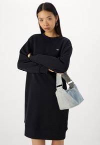 Svart sweatshirtkjole med ribbestrikkede mansjetter og nederkant, sammen med en lyseblå veske med tekstur og justerbar reim.