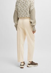Pull en maille raccourci avec un motif texturé beige, pantalon large crème, et baskets marron avec des accents crème et un logo.