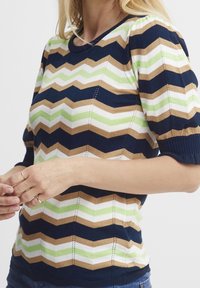 Pletený svetr s námořnickou modrou, zelenou, bílou a hnědou zigzagovou texturou. Krátké nabírané rukávy a pružné manžety. Texturované švy po celém produktu.
