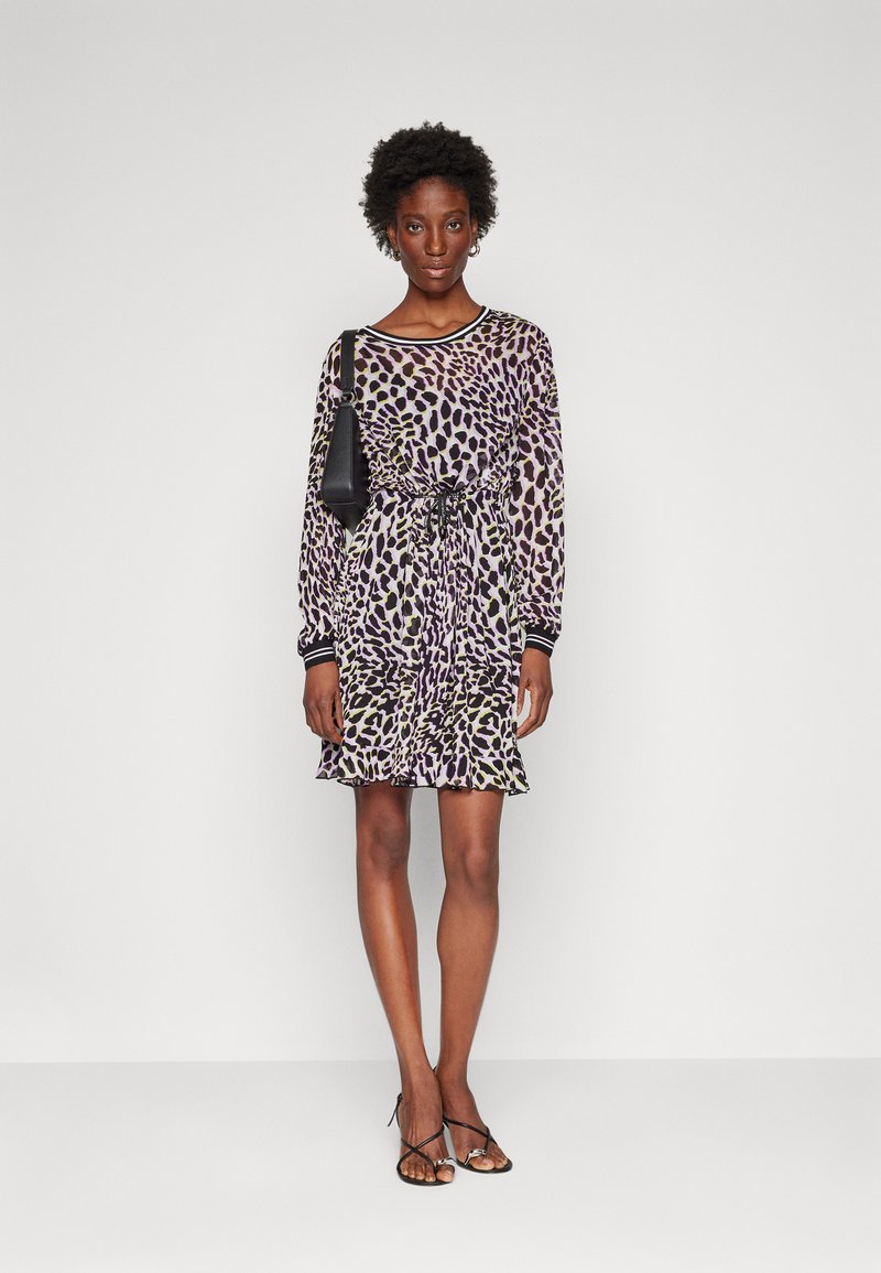 Floral-patterned dress in purple, green, and black. Features long sleeves, cinched waist, and ruffled hem. Paired with a small black bag.