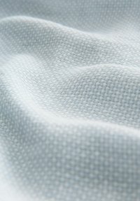 Svijetloplava tkanina s tkanim uzorkom koja prikazuje nježnu teksturu i suptilan mrežasti uzorak, s blagim nabranim i konturama za dodatni vizualni interes.