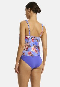 Jonge vrouw gezien vanaf de achterkant, met een bloemenmotief blauwe tankini top en paarse bikini broekjes, in een strandwaardige stijl.