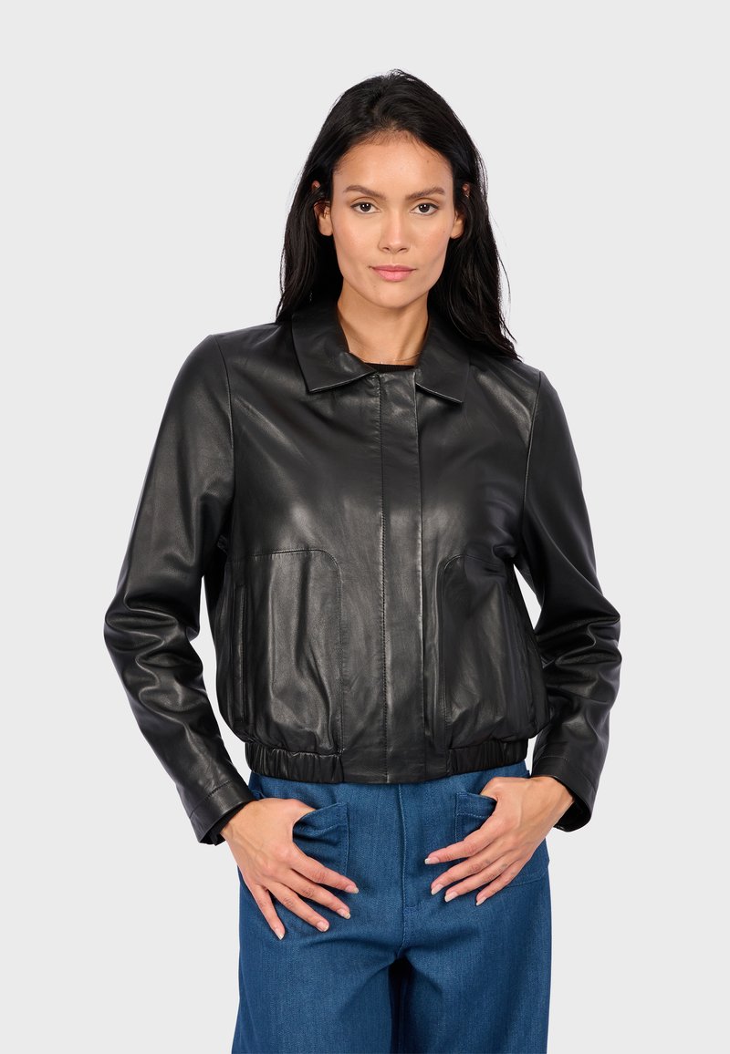 Černá kožená zkrácená bunda s límcem, předním zipem a velkými našitými kapsami. Hladká textura, přiléhavá v pase s elastickým pásem.