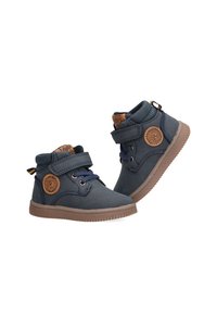 Zapatillas de tela azul con suelas de goma marrón, con una correa de velcro, parche de logo circular y detalles cosidos.