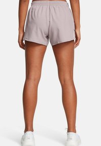 Pantalones cortos deportivos de color púrpura claro con cintura elástica, corte holgado y aberturas laterales, combinados con zapatillas deportivas blancas.