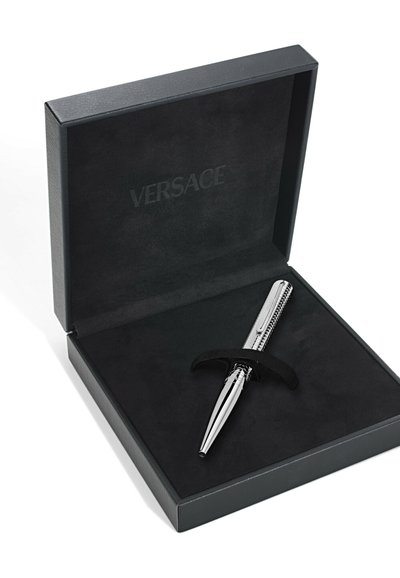 Stříbrné kovové pero s texturovaným úchopem, vystavené v černé krabičce s černou podšívkou. "VERSACE" je vyražené na vnitřní straně krabičky.