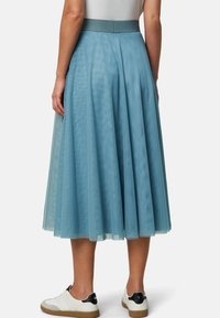 Une jupe midi plissée de couleur bleu clair, fabriquée en tissu transparent, avec une taille lisse, associée à des baskets blanches et un haut simple.