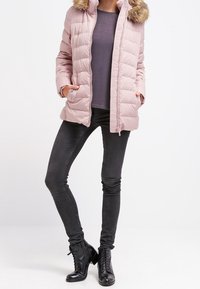 Ljusrosa puffjacka med dragkedja fram, huva och fuskpälsdetaljer. I kombination med en mörk topp och smala svarta jeans. Svarta snörboots.