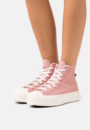 Růžové kotníkové kožené tenisky s bílými tkaničkami a gumovou podrážkou, s protexturovaným svrškem a neupraveným okrajem u límce pro detail.