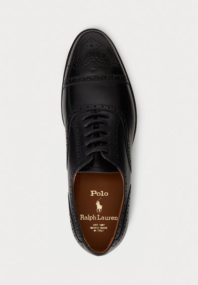 Scarpa da uomo in pelle nera con dettagli brogue, design con lacci e cuciture blu a contrasto. All'interno si può vedere una soletta marrone con il marchio.