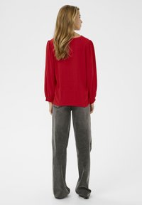 Rode blouse met pofmouwen, gestructureerde stof en een ronde halslijn; gecombineerd met losse grijze pantalons gemaakt van zachte geweven materialen.