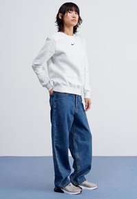 Szürke, nyakörv nélküli pulóver fekete logóval, laza, kék farmernadrággal és szürke sportcipővel párosítva. Az öltözet a laza és sportos elemeket egyesíti.