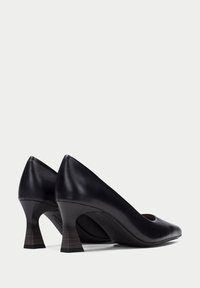 Pumps de cuero negro con punta redondeada y recortada, un tacón ligeramente cónico y un acento de madera texturizada en la base del tacón. Superficie lisa.