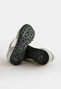 Schuhe mit einem grauen Wildlederoberteil, weißen Akzenten und einer schwarzen gummierten, profilierte Sohle, die für Traktion und Haltbarkeit ausgelegt ist.