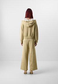 Dvojdelen outfit v metalno svetlo zlati barvi, ki vključuje skrajšan hoodie in široke hlače. Mehka tekstura in neobdelani robovi. Minimalističen dizajn.