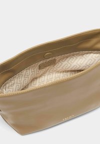 Torbica od tan umjetne kože s glatkom teksturom, s unutarnjim oblogom u geometrijskom uzorku. Zlatne oznake logotipa vidljive unutra.