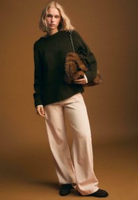Oversized dunkelgrüner Pullover, weite beigen Hosen aus weichem Material und eine Handtasche mit Fellakzenten. Akzente umfassen einen Kettenriemen und eine lässige Silhouette.