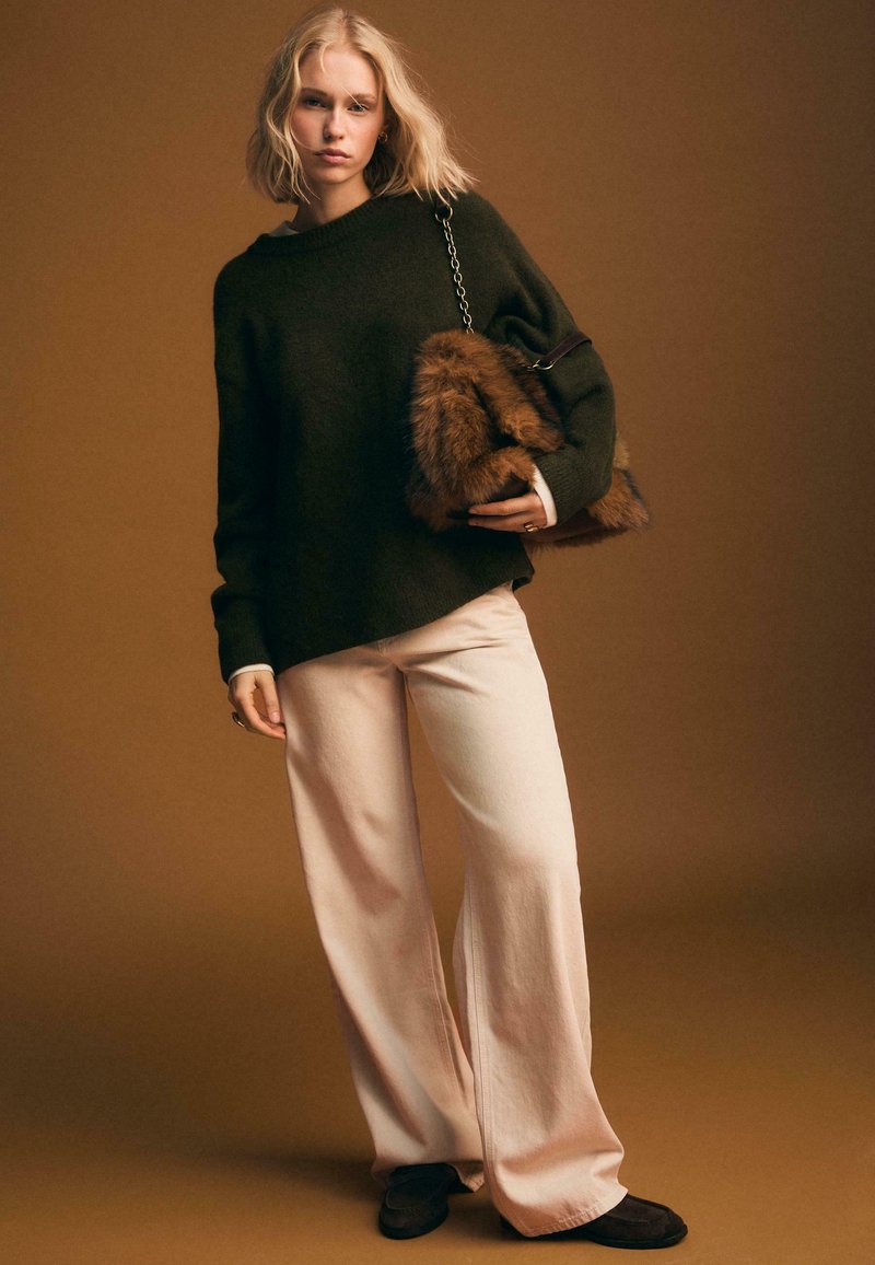 Oversized dunkelgrüner Pullover, weite beigen Hosen aus weichem Material und eine Handtasche mit Fellakzenten. Akzente umfassen einen Kettenriemen und eine lässige Silhouette.