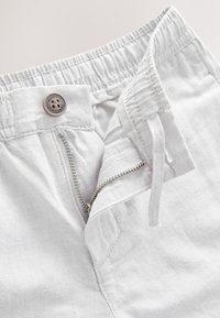 Białe spodnie z elastycznym paskiem w talii, zamkiem błyskawicznym i zapięciem na guzik. Wykonane z teksturowanej tkaniny o prostym designie.