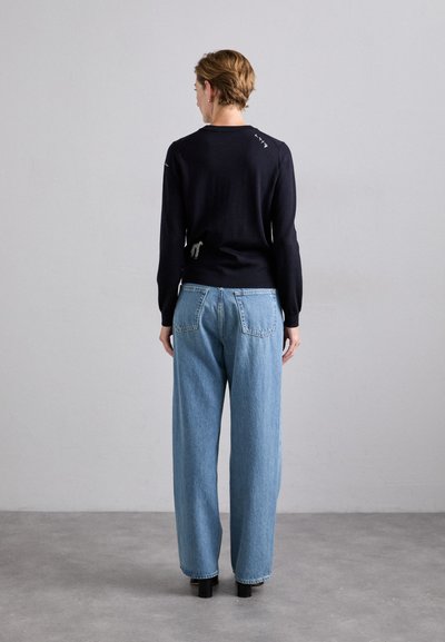 Mörkblå tröja med långa ärmar och stickat, ihop med ljusblå vida jeans. Outfiten har en unik detalj på baksidan.