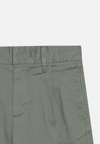 Zöld nadrág sima textúrával, slim fit szabással, elülső zsebekkel és lapos derékpánttal, amelyen kontrasztos varrási részletek találhatók.