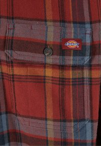 Red and gray plaid flannel shirt with a buttoned pocket, featuring yellow and blue accents; includes a Dickies brand label.