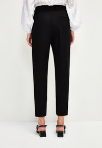 Svarta skräddarsydda byxor med slim fit, med en slät textur, bakfickdetalj och kort längd, i kombination med blockklackade sandaler.