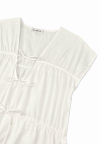 Hvit bluse med V-hals, korte ermer og strikket midje. Laget av myk stoff med rynkedetaljer og sløyfe-akkenter.