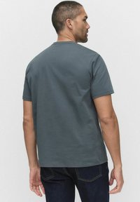 Grå kortärmad t-shirt i bomull med rund halsringning, slät textur och avslappnad passform, sedd bakifrån, i kombination med mörka jeans.