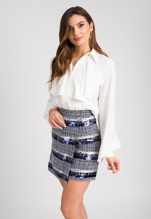 Biała bluzka z długim rękawem i falbanianym kołnierzem, połączona z dopasowaną, wielokolorową spódnicą z cekinami w paski w kolorach srebrnym, niebieskim i granatowym.