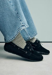 Zwarte suède moccasin schoenen met veters, gedragen met grijze gemêleerde sokken, gecombineerd met lichtblauwe wijde jeans.