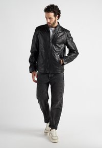 Zwarte leren jas met een hoge kraag, ritssluiting en zijzakken. Draag het met donkere jeans en witte sneakers, met subtiele textuurdetails.