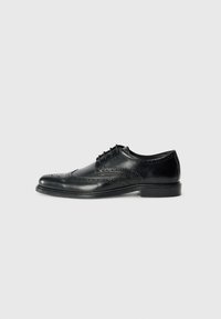 Chaussure habillée en cuir noir avec des détails en brogue, une finition lisse, un système de laçage et un petit talon. Design classique et formel.
